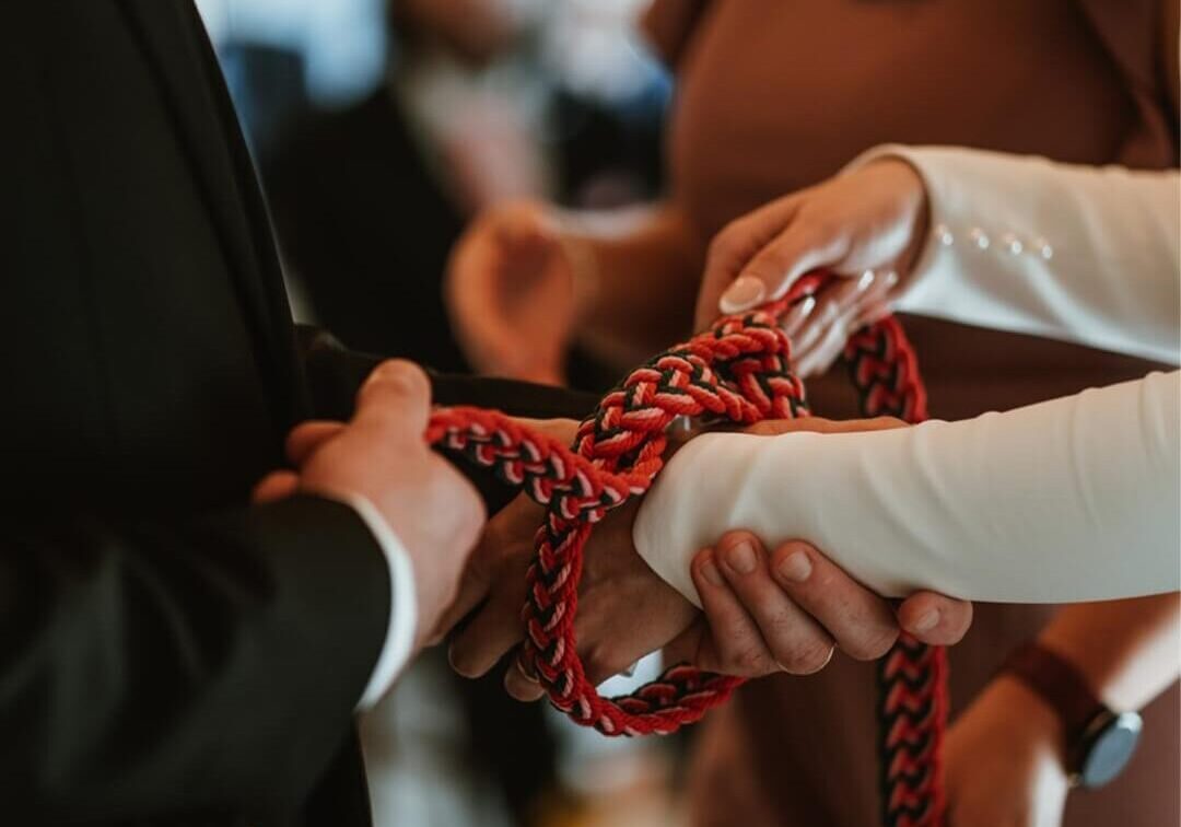Close up of a bride and grooms hands being tie in a handfasting ceremony